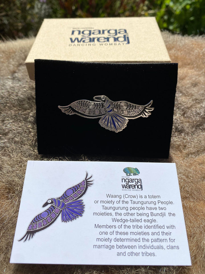 Add a finishing touch to any outfit, with this Lapel Pin featuring a Waang the Crow design by Ngarga Warendj Dancing Wombat Measures 26.5mm x 60mm  Presented in a stylish box with magnetic closure  Made with metal with enamel inlay Includes an information card on the design and artist