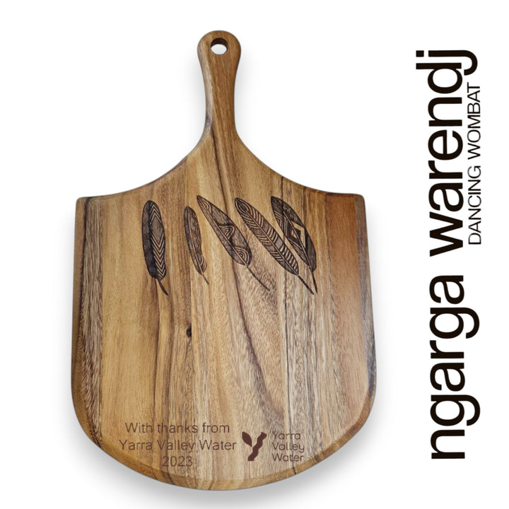 Wooden cutting board with engraved feathers and 'Yarra Valley Water' branding on a white background.