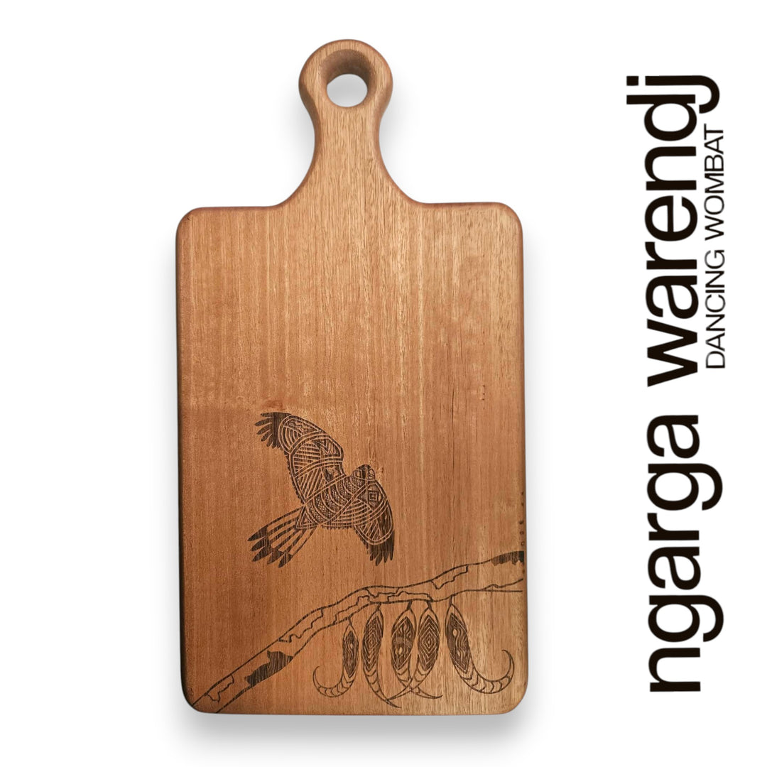 Wooden cutting board with engraved design of a bird and tree branch, branded 'ngarga warendj'.