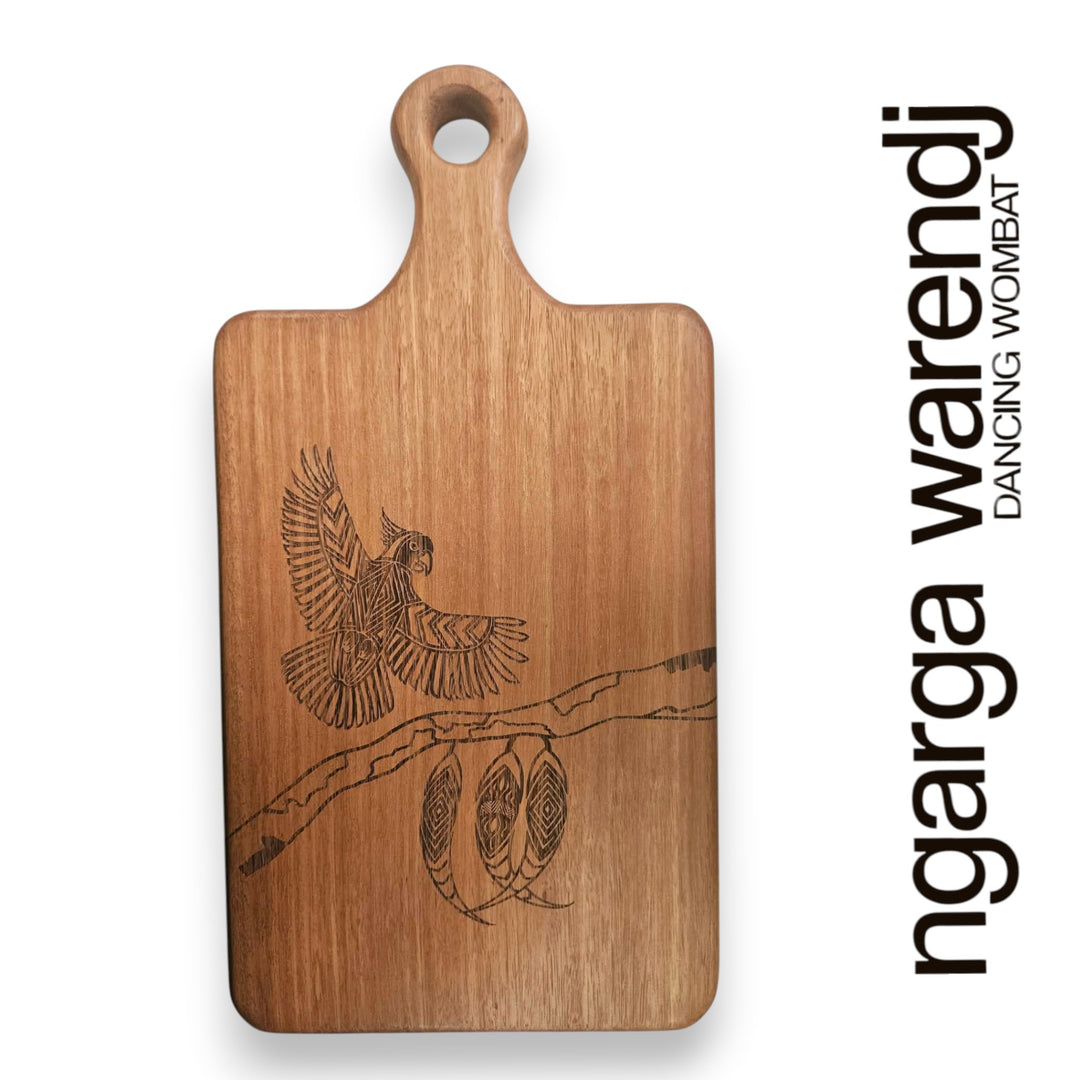 Wooden cutting board with engraved design of a bird and gum leaves branch, branded 'ngarga warendj'.
