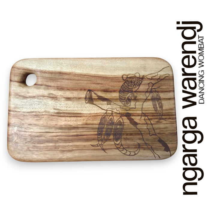 Wooden cutting board with laser engraving of a koala and text 'ngarga warendj Dancing Wombat' on a white background.