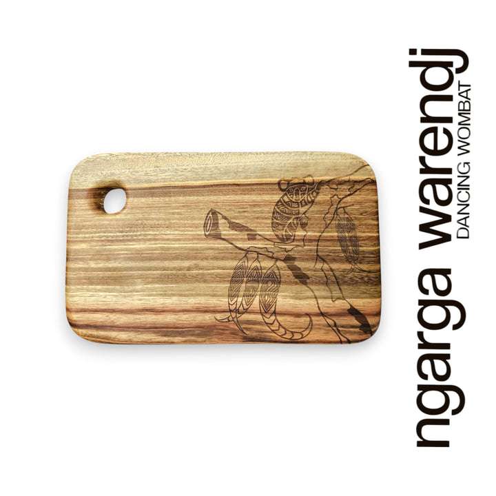 Wooden cutting board with laser engraving of a dancing wombat design on a white background, featuring the brand 'ngarga warendj'.