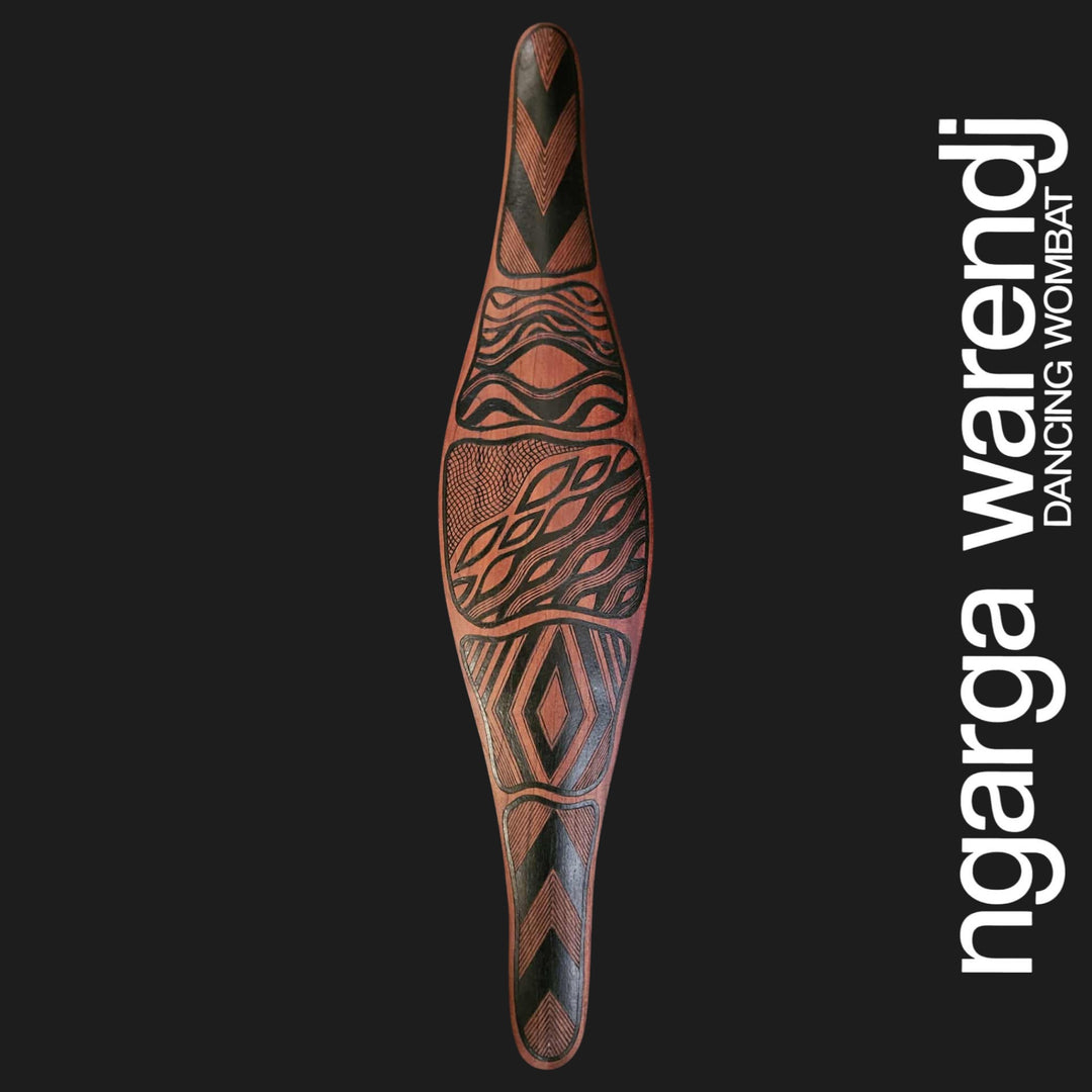 Decorative wooden tool with tribal patterns on a black background, featuring the brand 'ngarga warendj'.