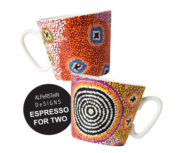 Two ceramic espresso mugs with Aboriginal dot art patterns, shown on a white background with a black circular badge that reads 'ALPerStein DeSIGNS ESPRESSO FOR TWO'. The mugs feature vibrant multicolor designs, including one with orange, red, white, and blue dots, and another with black, white, yellow, and purple concentric dots.