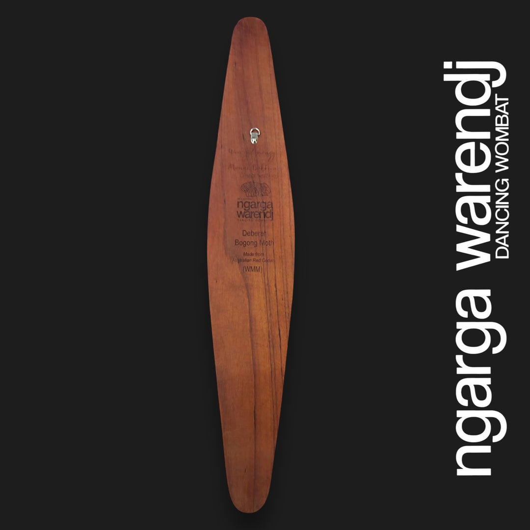 A long, narrow wooden board or plaque with a warm brown wood grain and engraved text, centered on a black background. Large white vertical text along the right side reads 'ngarga warendj DANCING WOMBAT'.