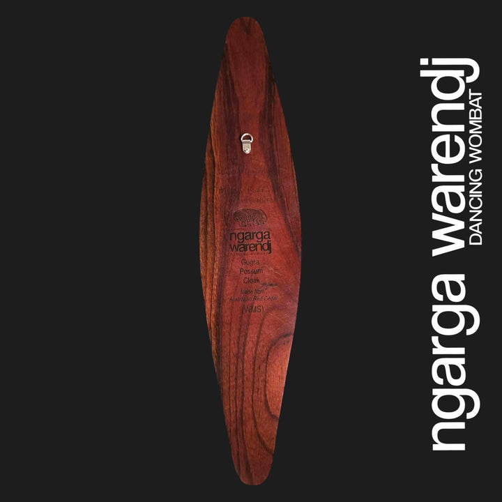 Back of small Gugra Possum Cloak wall shield showing red cedar grain, metal wall hanger and Ngarga Warendj maker mark.