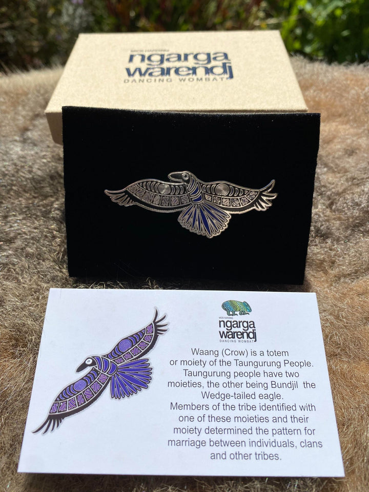 Add a finishing touch to any outfit, with this Lapel Pin featuring a Waang the Crow design by Ngarga Warendj Dancing Wombat Measures 26.5mm x 60mm  Presented in a stylish box with magnetic closure  Made with metal with enamel inlay Includes an information card on the design and artist 