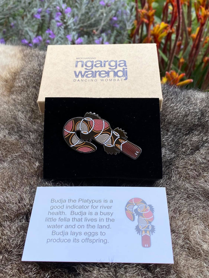Add a finishing touch to any outfit, with this Lapel Pin featuring Budja the Platypus design by Ngarga Warendj Dancing Wombat  Measures 60 mm x 32.2mm  Presented in a stylish box with magnetic closure  Made from metal with an enamel inlay Information card included - with information on the design and artist 