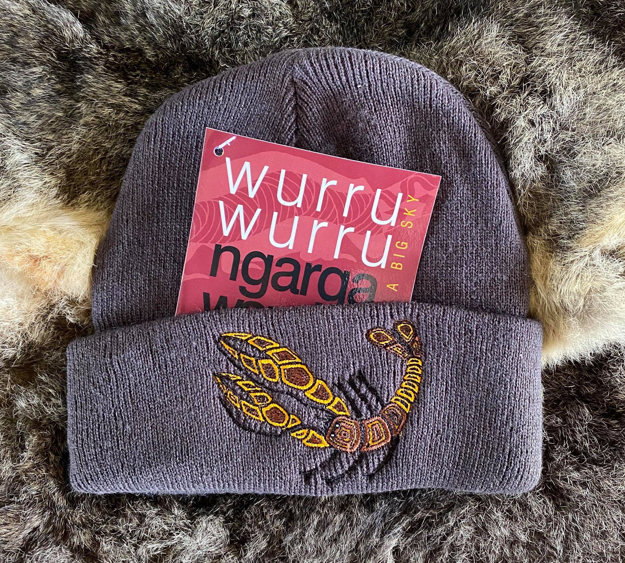 Ngarga Warendj Slate Grey Beanie with Embroidered Brown & Yellow Yabby Design   Bunggan Gulum the Yabby lives in wetlands, rivers, creeks, dams   and waterways. He builds his mud brick home for protection from   the elements and from predators.  He makes very good tucker   when boiled up.  